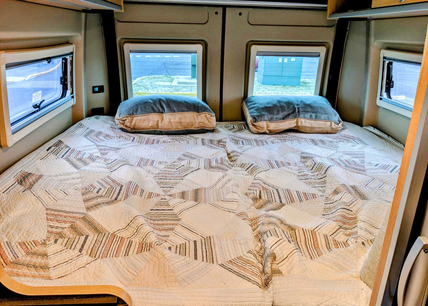 Cozy RV rental bedroom with a patterned quilt, two pillows, and windows.