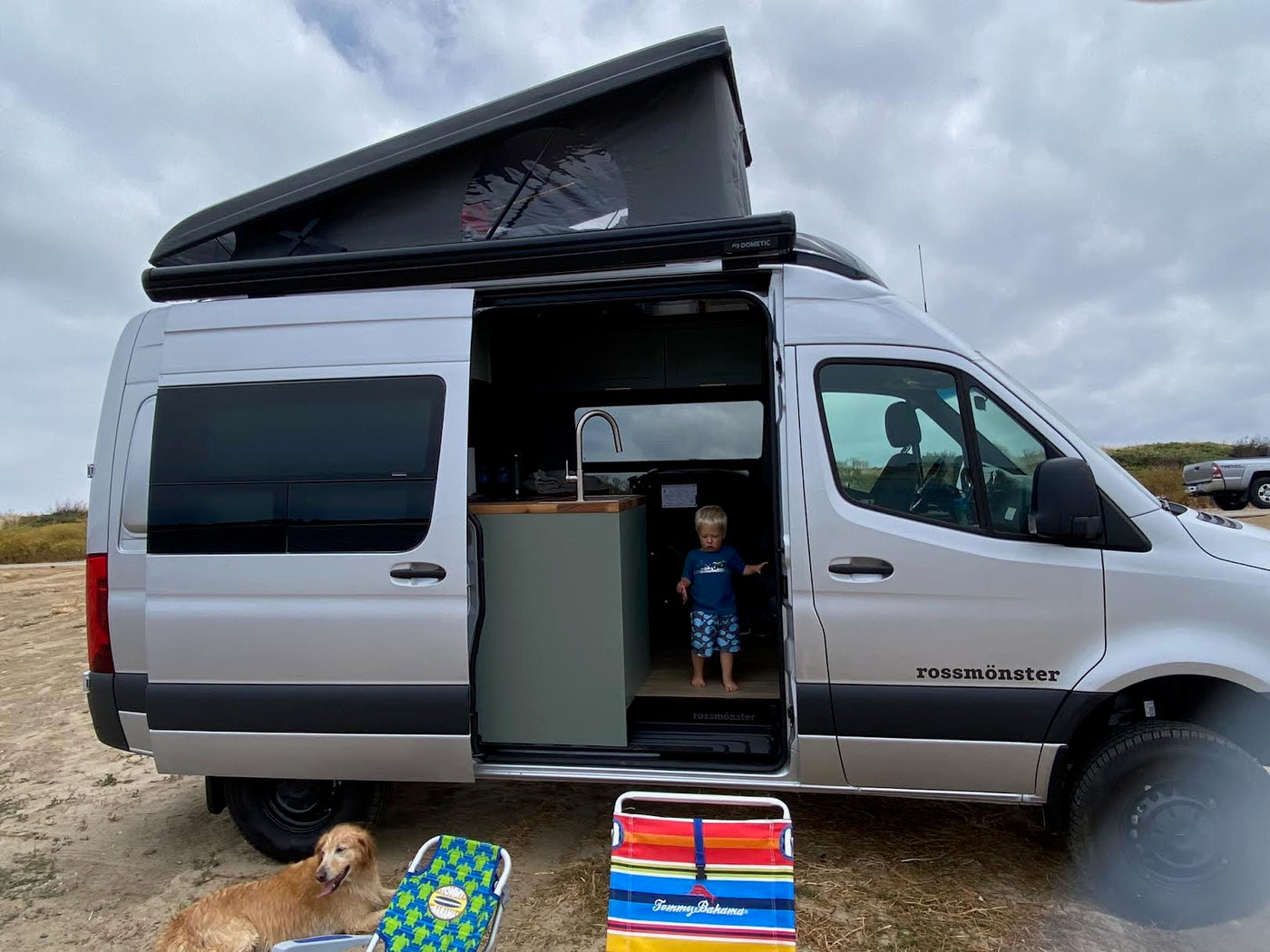  parked on sand. Shows the interior kitchen and pop-top.|Cozy rv rental interior: dining table with croissants & two seats — photo 4