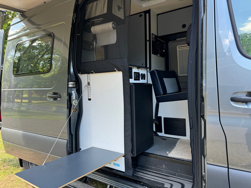 Gray **RV rental** van with open sliding door reveals organized interior: kitchen, controls, passenger seat & pull-out outdoor table. — photo 6