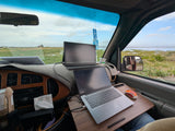 Work from your RV rental! This mobile office features a laptop, portable monitor, and coffee, overlooking scenic waters.