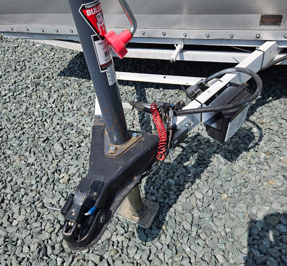 An RV rental trailer's hitch, jack, safety chains, and electrical wiring on gravel. A low voltage warning is visible. — photo 18