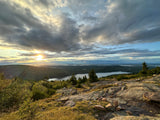 A vibrant sunset casts rays over a vast forested landscape and tranquil lake, ideal for an RV rental getaway.