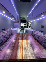 RV rental interior: A stylish living area with a large wood table, cushioned seating, kitchen, and accent LED lighting.