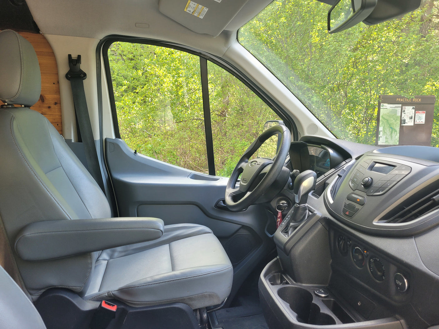 Inside an RV rental van: driver's seat, steering, dashboard, and nature view. Ready for your next adventure.