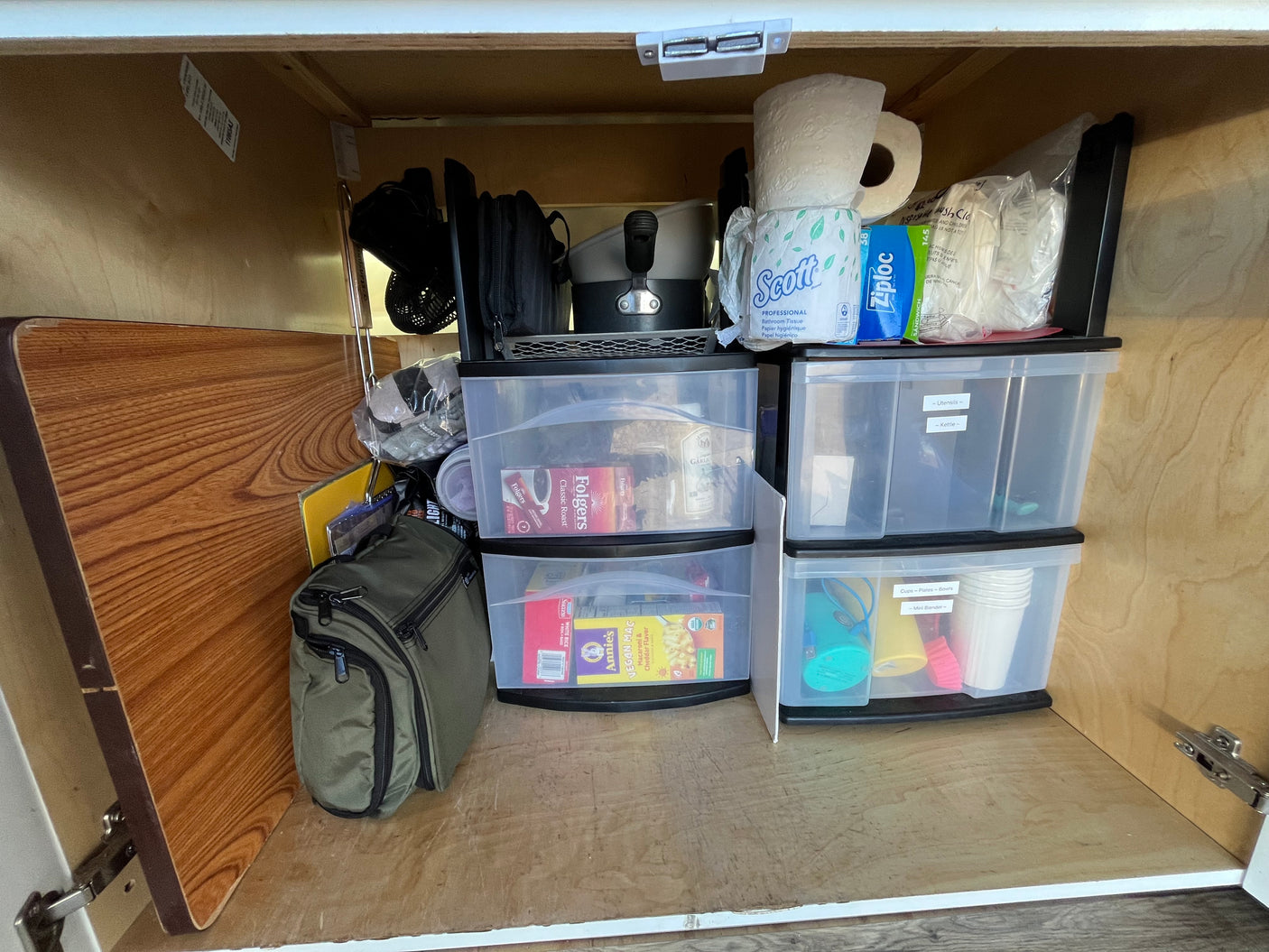 RV rental cabinet: smartly organized with labeled clear bins for kitchenware, food, & supplies like toilet paper.