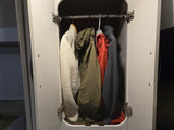 Inside an RV rental: a compact closet with a white fleece, olive jacket, red jacket, and grey fleece hanging.