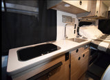 Modern RV rental interior: a functional kitchen with sink, stovetop, and clean countertops, beside a comfy bed.