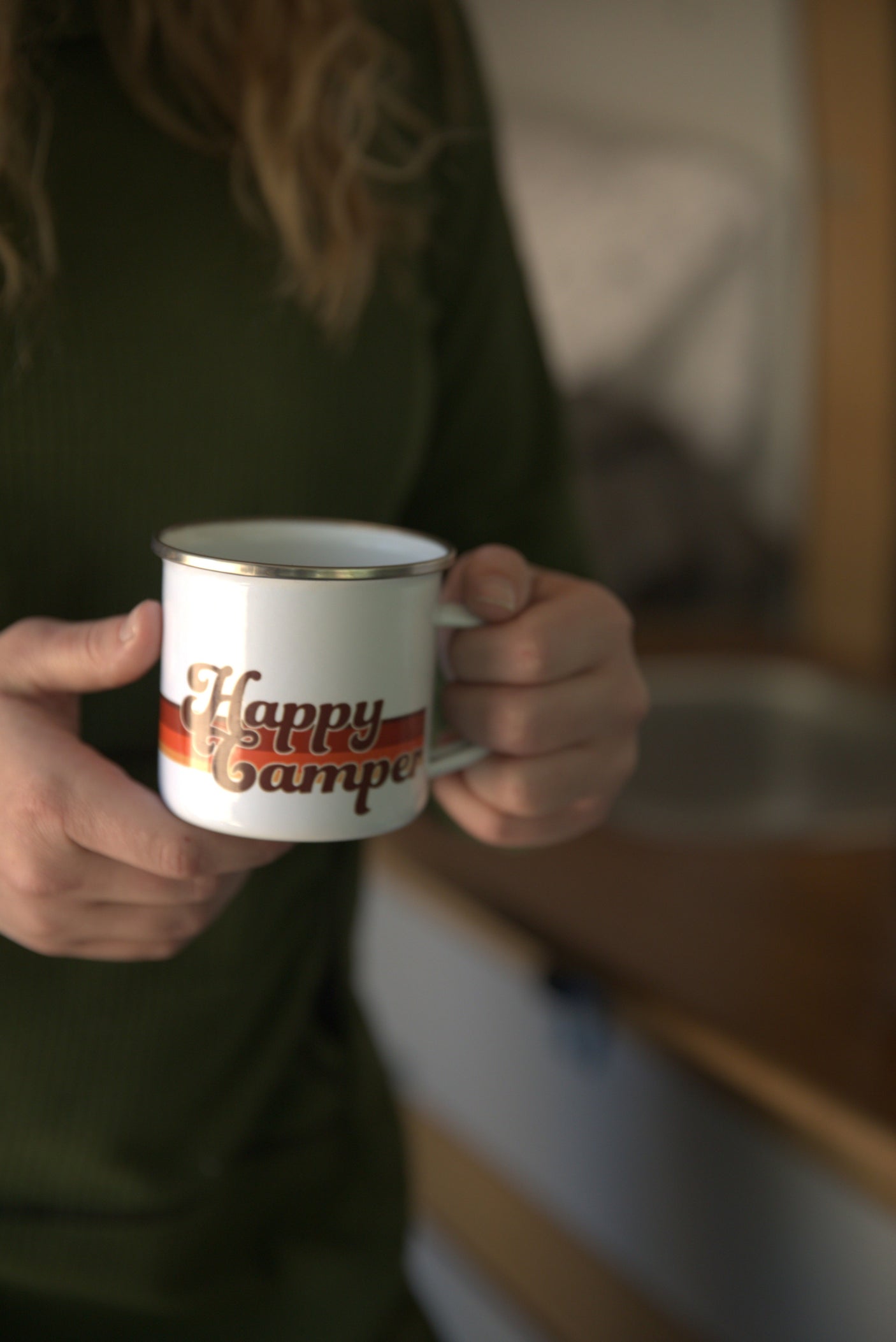 Enjoying a warm drink from a "Happy Camper" mug inside a cozy RV rental.