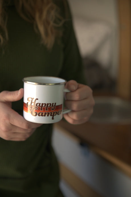 Enjoying a warm drink from a "Happy Camper" mug inside a cozy RV rental.