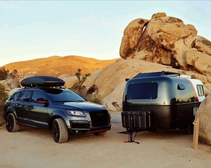 An Audi SUV with roof box tows a modern teardrop camper, an ideal RV rental for a luxury desert adventure among rocks. — photo 1