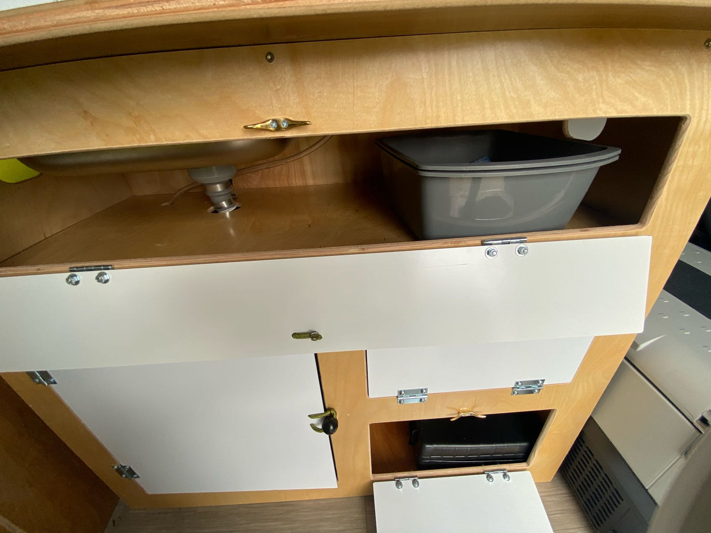 Light wood RV rental interior showing a functional sink area with a removable basin and multiple storage cabinets.
