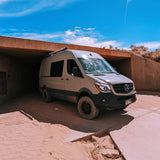A rugged, off-road rv rental Mercedes Sprinter van navigates a sandy underpass. Perfect for desert adventures!