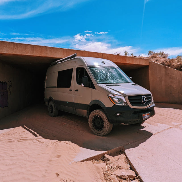 A rugged, off-road rv rental Mercedes Sprinter van navigates a sandy underpass. Perfect for desert adventures!