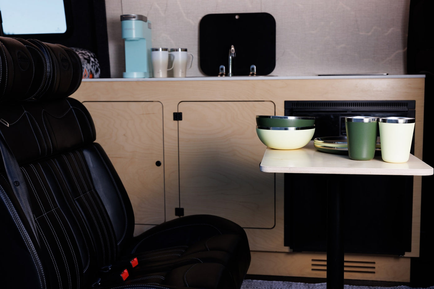 Inside a cozy RV rental: black leather captain's chair, fully equipped kitchenette with coffee maker, and dining area with modern dishes. — photo 5