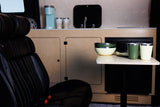 Inside a cozy RV rental: black leather captain's chair, fully equipped kitchenette with coffee maker, and dining area with modern dishes.