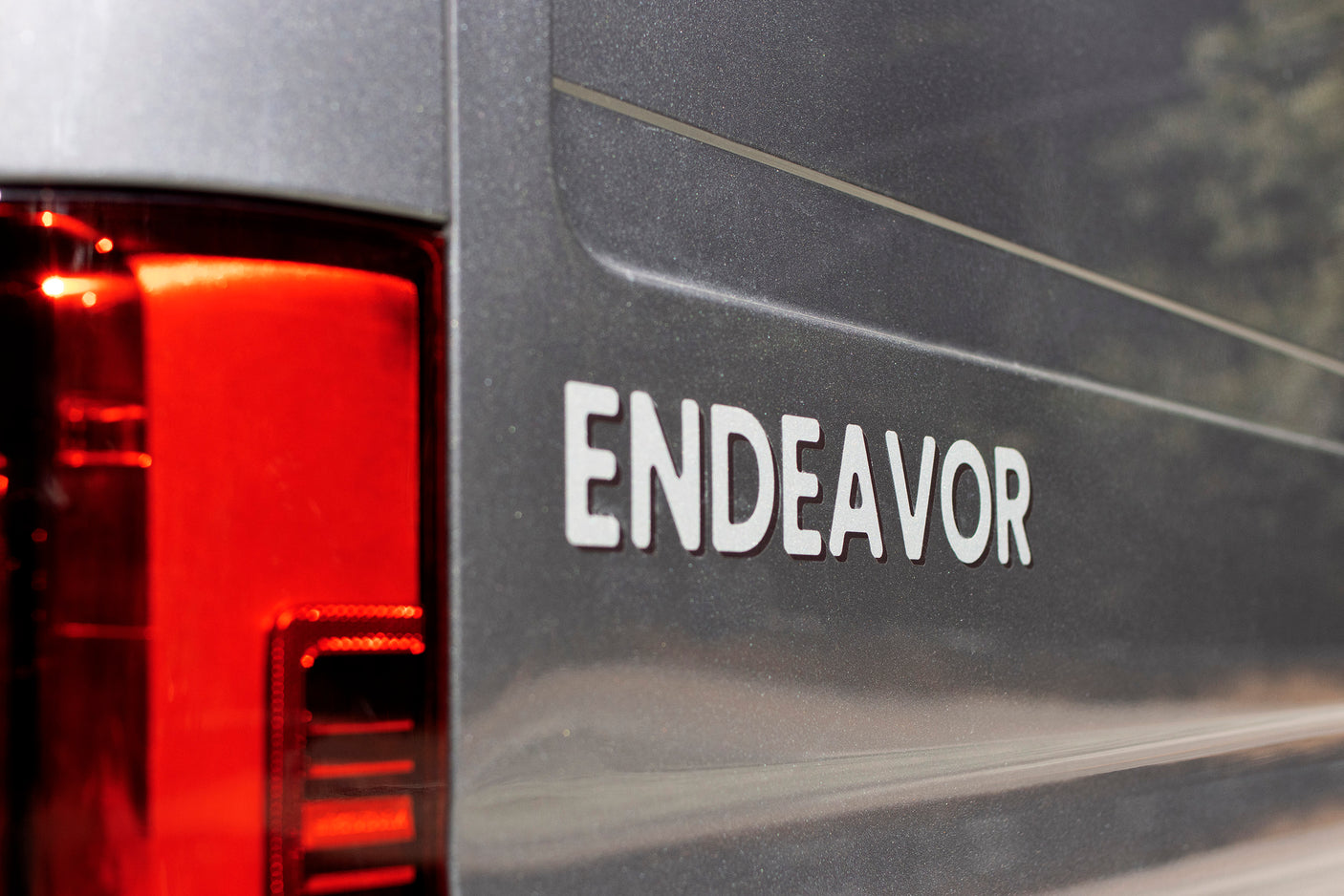 Rear view of an "ENDEAVOR" RV rental featuring a bright red taillight and dark grey exterior. Ready for your next travel adventure.
