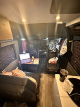 Inside an RV rental: a compact living space with a laptop workspace, kitchen counter, and driver's area.