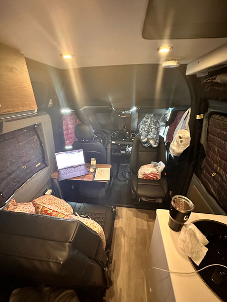 Inside an RV rental: a compact living space with a laptop workspace, kitchen counter, and driver's area.