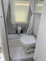 Inside an RV rental: a compact white wet bath featuring a toilet, shower, and curtain for efficient travel.