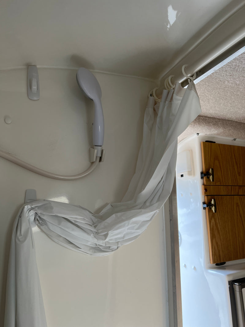 RV rental shower: white shower head, hose, and curtain secured by Command hooks. Features white walls and adjacent wooden cabinets. — photo 4