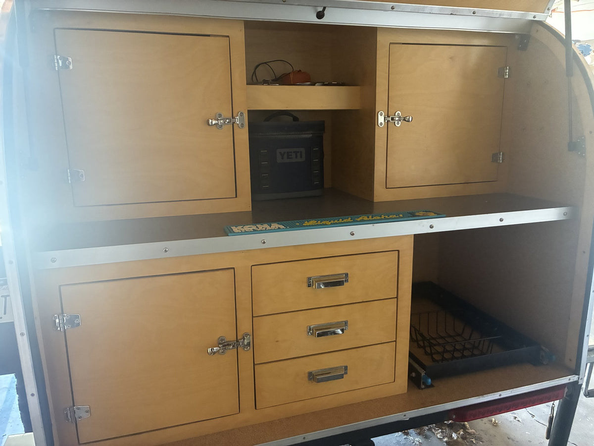 Rear galley with the hatch open: birch cabinet doors, three drawers, a slide-out basket and open counter space — photo 4