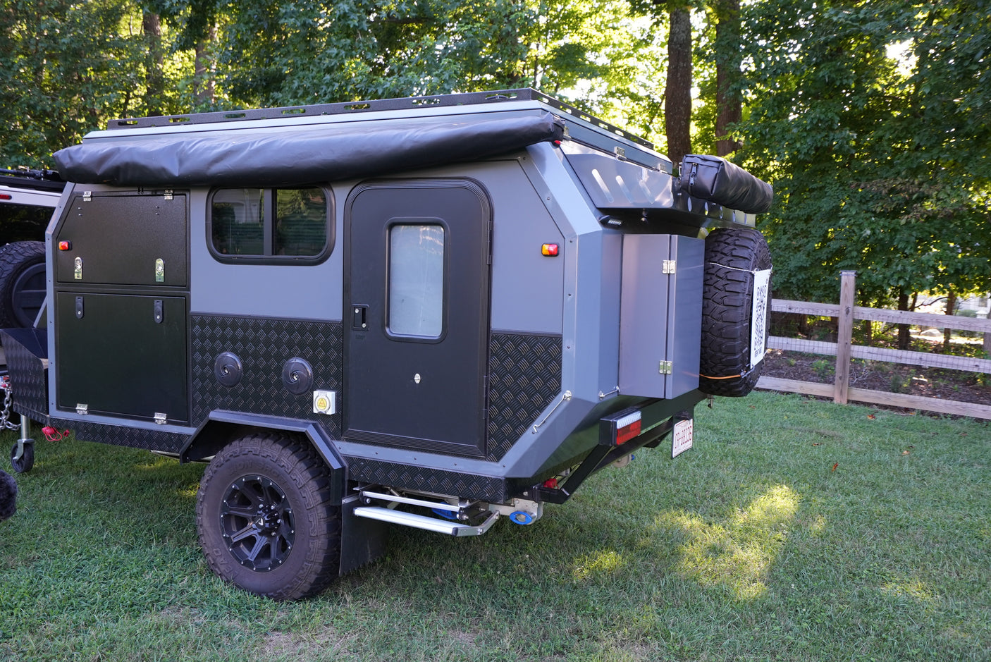 Discover this compact overland trailer, a perfect rv rental for adventures! Gray & black design, off-road tires, parked on grass.