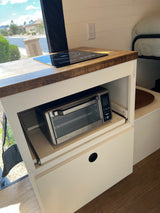 Efficient RV rental kitchen: induction cooktop, pull-out Gourmia toaster oven, and adjacent sleeping area.