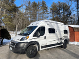  parked on a snowy driveway near bare and evergreen trees.|RV rental interior: ladder to pop-top