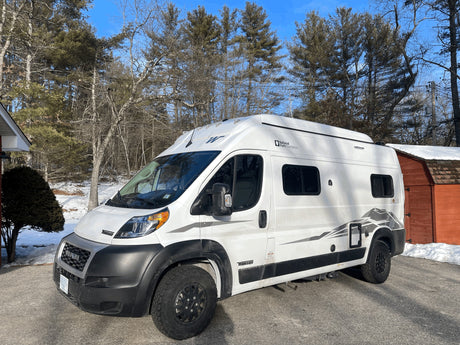  parked on a snowy driveway near bare and evergreen trees.|RV rental interior: ladder to pop-top