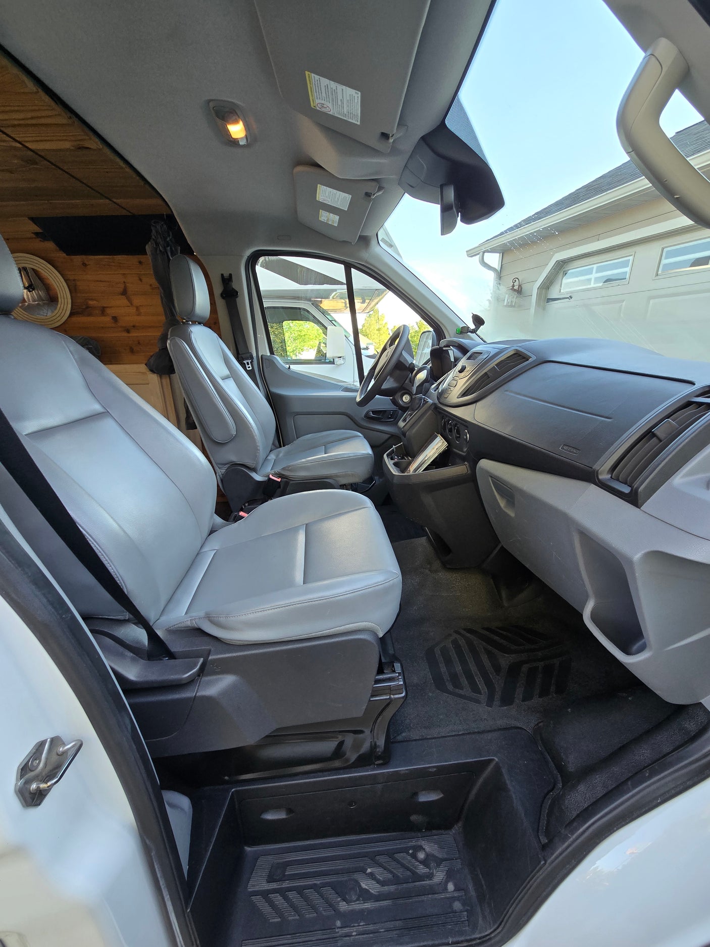 Spacious front cabin of an RV rental camper van, featuring grey seats, dashboard, and custom wood paneling.