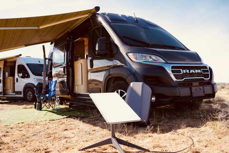 This rv rental is ready for adventure! A dark grey camper van with awning and a Starlink dish are set up in a dry, open landscape.