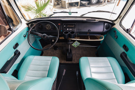 Explore the vintage charm of this RV rental: bright teal and white seats, classic dashboard, and gear shift inside.