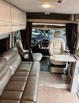 Modern RV rental interior: view of the living area with a taupe sofa, cream cab seats, and a swivel table.