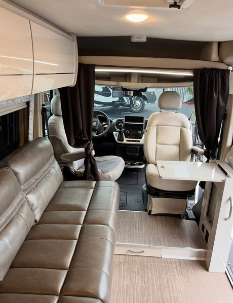 Modern RV rental interior: view of the living area with a taupe sofa, cream cab seats, and a swivel table.