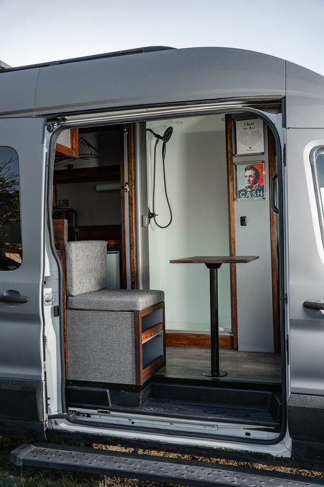 Inside an RV rental: a gray camper van's open side door reveals a cozy interior with a bench seat, table, and shower.