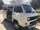 Classic white VW camper van, side door open, awning deployed. Ideal RV rental for road trips.