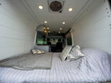 Cozy RV rental interior with a bed, kitchenette, and wood paneling, seen from the back.
