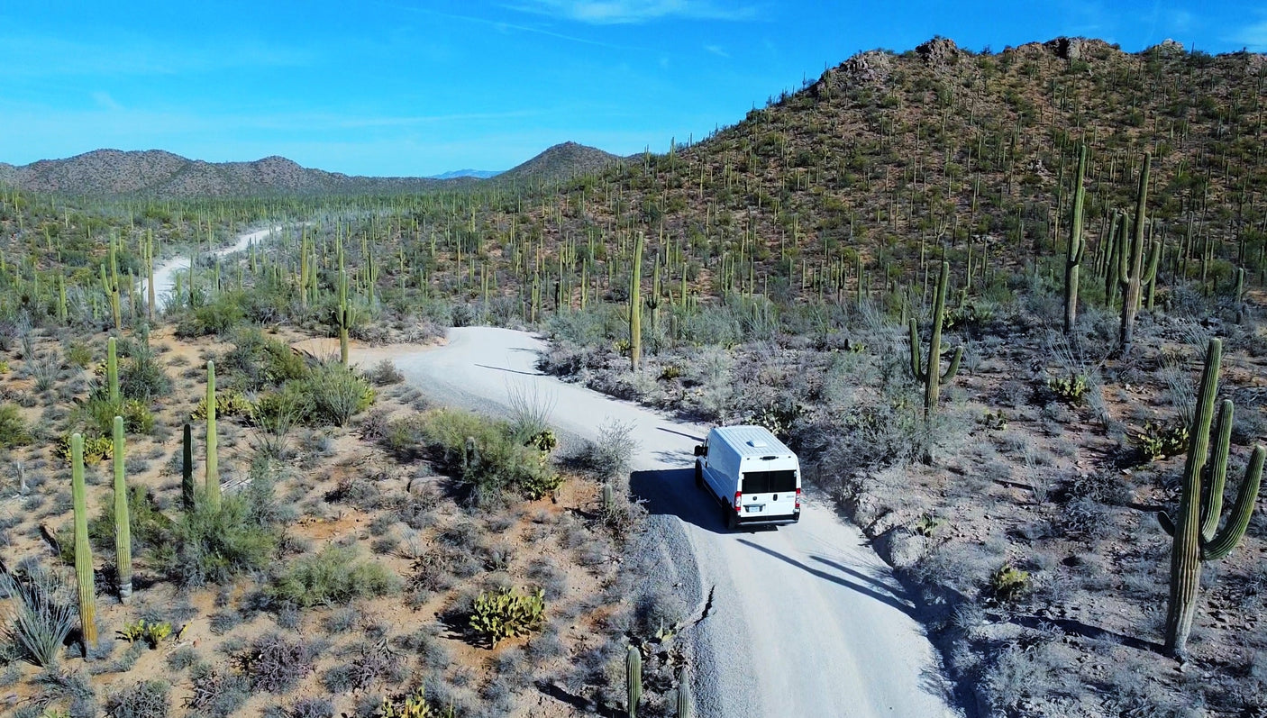 A white RV rental van winds through a stunning desert landscape filled with saguaro cacti.