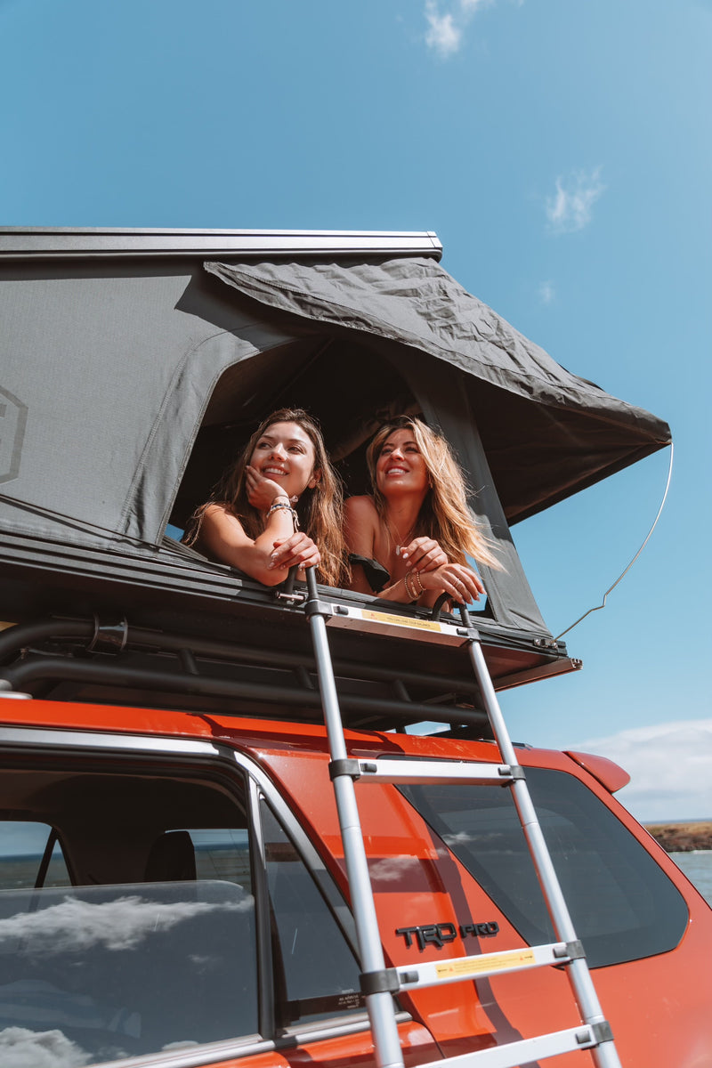 Two women smile from a rooftop tent on an orange RV rental SUV with a ladder, enjoying the view. — photo 8