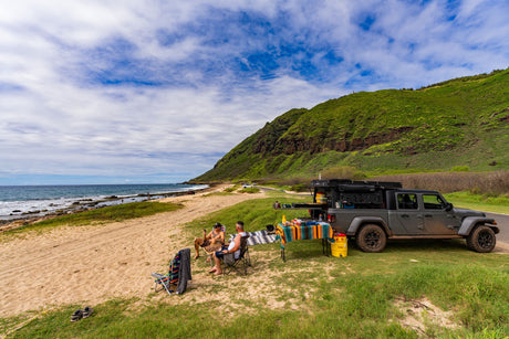 A rugged RV rental, a customized Jeep Gladiator, at a scenic beach campsite with two men relaxing by the sea.