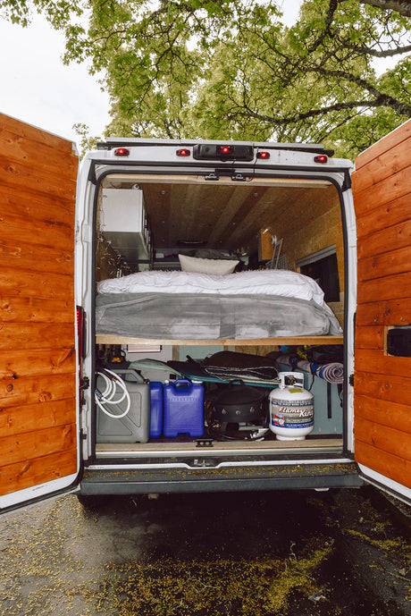 Inside a custom RV rental: The back of this camper van shows a raised bed over organized storage, ready for any road trip.