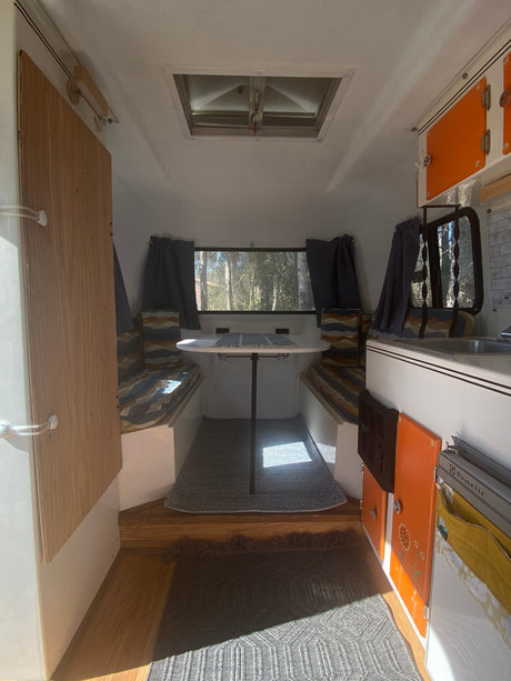 Interior view of an RV rental, showing a well-lit dinette, kitchen area, and patterned rugs. Ready for your next road trip.