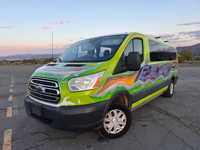 Vibrant custom-painted Ford Transit van with graffiti art, possibly an rv rental, parked outdoors with mountains and city in the background.