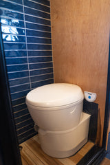 RV rental bathroom with a white Thetford RV toilet, blue subway tiles, wood walls, and slatted wood floor.