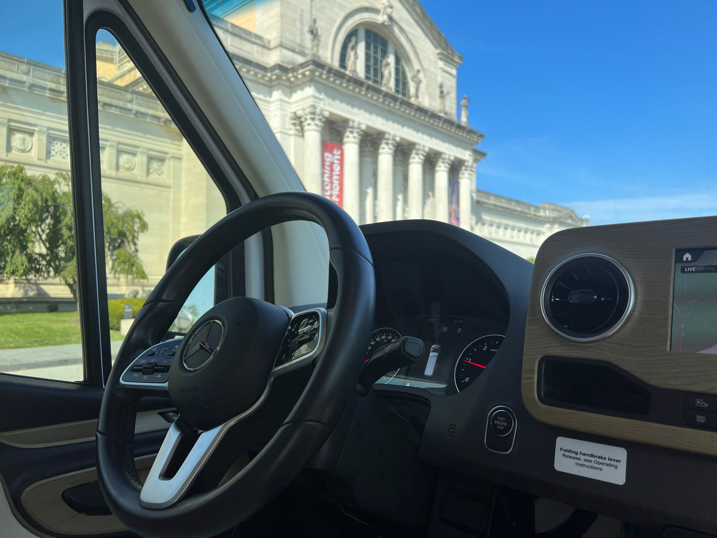 Inside a Mercedes rv rental, showcasing the steering wheel and dashboard, with a classical museum outside.