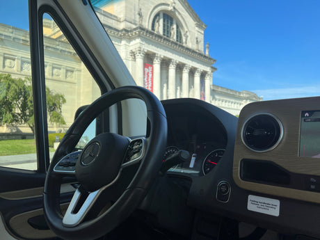 Inside a Mercedes rv rental, showcasing the steering wheel and dashboard, with a classical museum outside.