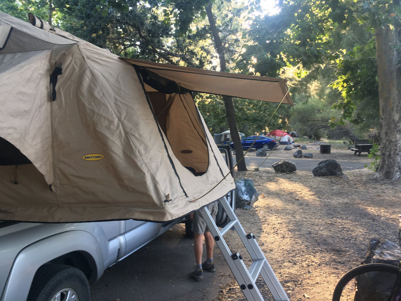 Side view of the open tent showing the yellow Smittybilt badge, extended awning, guy line and zippered mesh door — photo 5
