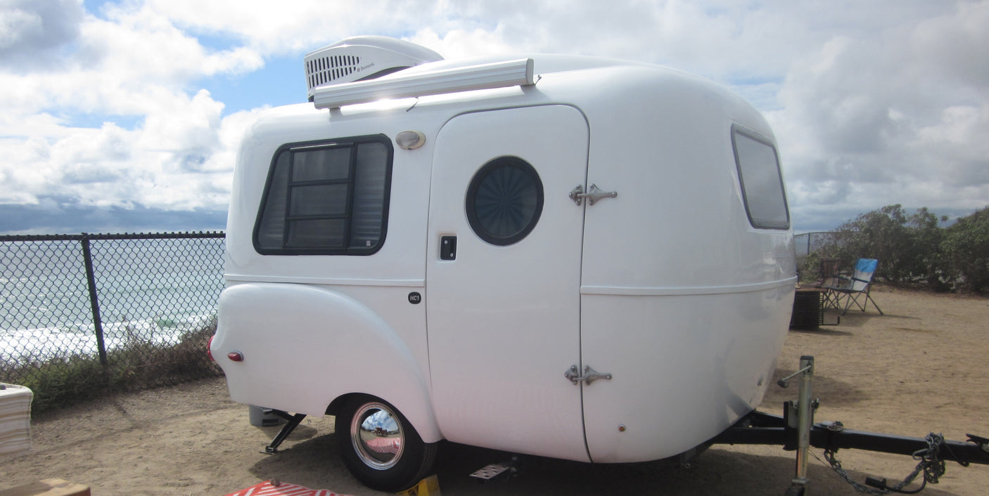 Oceanfront RV rental: A sleek white teardrop trailer with an AC unit, parked steps from the ocean for seaside camping.