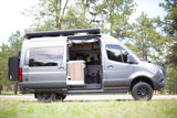 This grey Storyteller Overland camper van, perfect for RV rental adventures, is parked with its side door open revealing the interior.