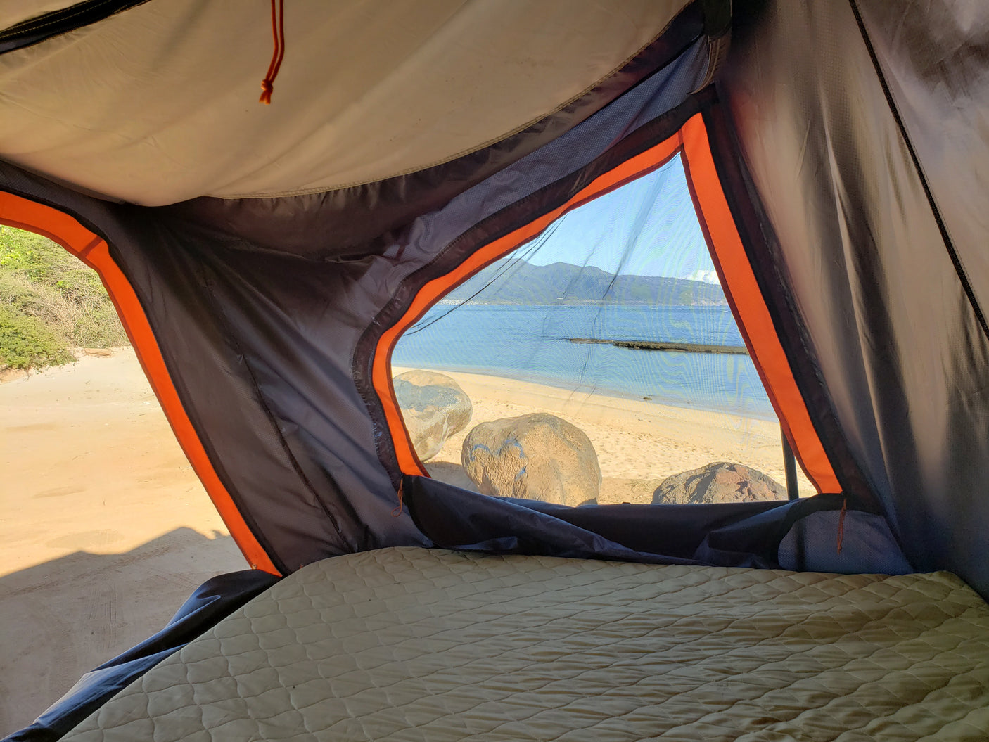 Wake up to this! Inside an RV rental's cozy tent, a comfy mattress provides a panoramic view of a sunny beach and ocean.